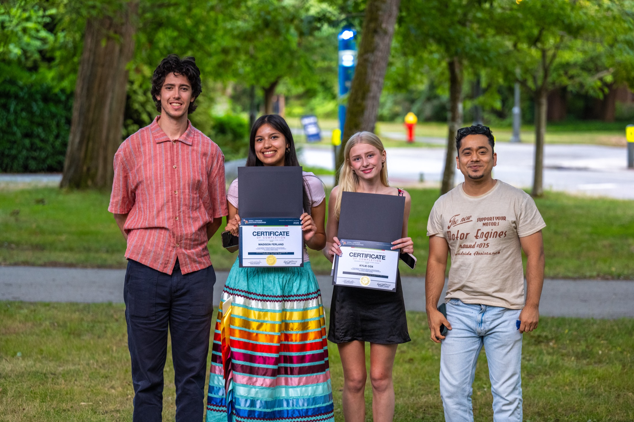 Four Kirkness Scholars holding their program certificates outdoors on campus