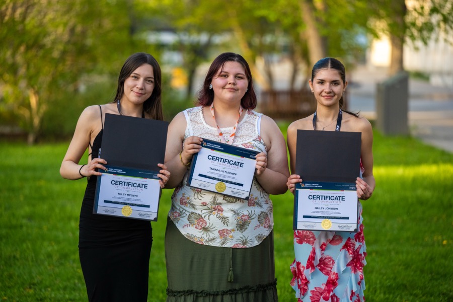 Three Kirkness Scholars holding their certificates on the grass
