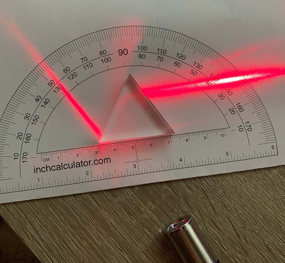 Photo of a glass triangle placed in the middle of a protractor reflecting a red light.
